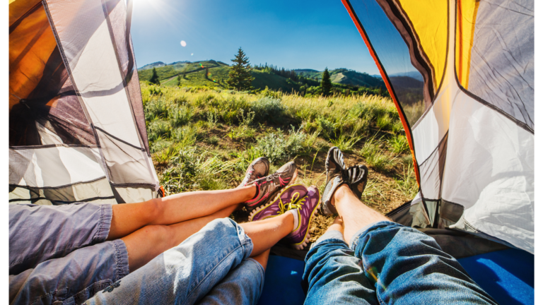 Image of the outdoors from the viewpoint of a camper lying in a tent. Image shows three sets of legs and the nature beyond.