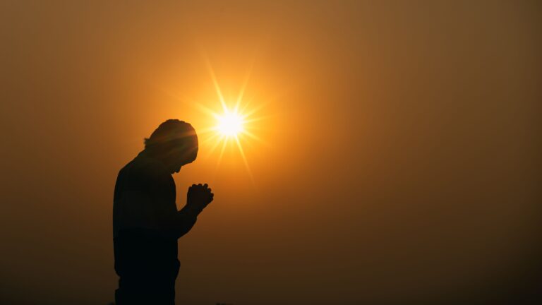 Man Praying in front of a sunset to God.