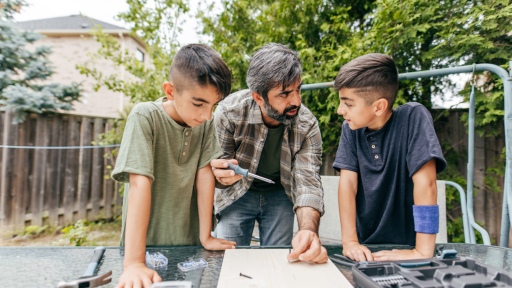 Dad teaching sons to build wooden item outdoors.